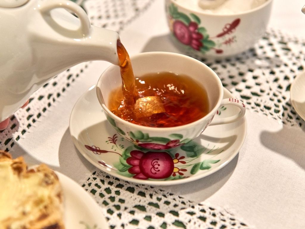 In einer Tasse mit Teerose befindet sich an Kluntje. In diese Tasse wird Tee gegossen.